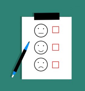 Survey clipboard with a blue pen against a green background with three options from top to bottom - neutral face, smiley face and sad face